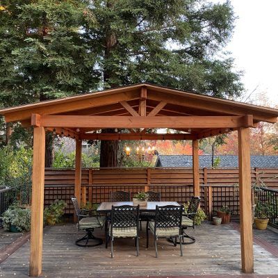 A chandelier hangs under a backyard pergola designed for luxury dining and outdoor entertainment